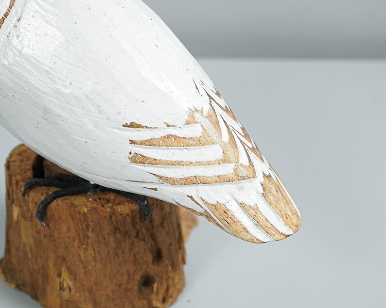 K&ouml;nnte beinhalten: Geschnitzte Holzfigur eines Vogels, wei&szlig; bemalt mit gewischten Details. Der Vogelk&ouml;rper sitzt auf einem kleinen, nat&uuml;rlichen Holzsockel. Die F&uuml;&szlig;e des Vogels sind schwarz. Das Design hat eine rustikale, handwerkliche &Auml;sthetik.