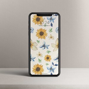 Könnte beinhalten: Ein schwarzes Smartphone mit einer floralen Tapete mit gelben Sonnenblumen und blauen Blumen. Die Uhrzeit ist 10:24 Uhr und das Datum ist Dienstag, 13. September.