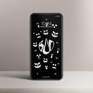Könnte beinhalten: Ein schwarzes Smartphone zeigt einen Halloween-Themen-Sperrbildschirm. Der Bildschirm zeigt weiße Illustrationen von Kürbisgesichtern und das Wort "BOO". Die Uhrzeit ist 10:24 Uhr, Dienstag, 13. September.