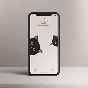 Könnte beinhalten: Ein schwarzes iPhone mit weißem Hintergrund und zwei schwarzen Katzen, die aus den oberen Ecken schauen. Die Uhrzeit ist 10:24 Uhr und das Datum ist Dienstag, 13. September.