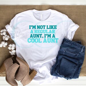 May include: White t-shirt with the text "I'M NOT LIKE A REGULAR AUNT, I'M A COOL AUNT" in blue and teal text.