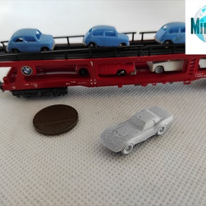 Puede incluir: Un vag&oacute;n de tren rojo de juguete con una plataforma que lleva cuatro coches de juguete azules. El vag&oacute;n de tren tiene un logotipo de BMW y el texto "MiniCust Miniatures Custom". Un coche de juguete plateado est&aacute; en primer plano.
