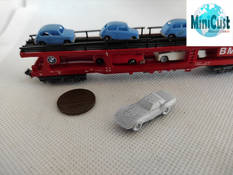 Puede incluir: Un vag&oacute;n de tren rojo de juguete con una plataforma que lleva cuatro coches de juguete azules. El vag&oacute;n de tren tiene un logotipo de BMW y el texto "MiniCust Miniatures Custom". Un coche de juguete plateado est&aacute; en primer plano.