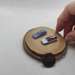 May include: Two miniature toy cars on a wooden base. The car on the left is a light blue and white police car. The car on the right is a red and white ambulance. A penny is in the foreground.