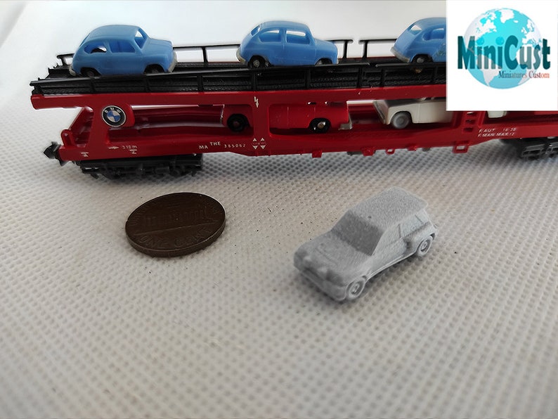Puede incluir: Un vag&oacute;n de tren de juguete rojo con una plataforma que transporta tres coches de juguete azules. El vag&oacute;n de tren tiene un logotipo de BMW en el lateral. Un coche de juguete gris est&aacute; sentado en una superficie blanca delante del vag&oacute;n de tren.