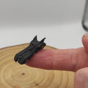 Puede incluir: Un pequeño coche de juguete de metal negro con forma de Batmóvil de la franquicia de películas de Batman.