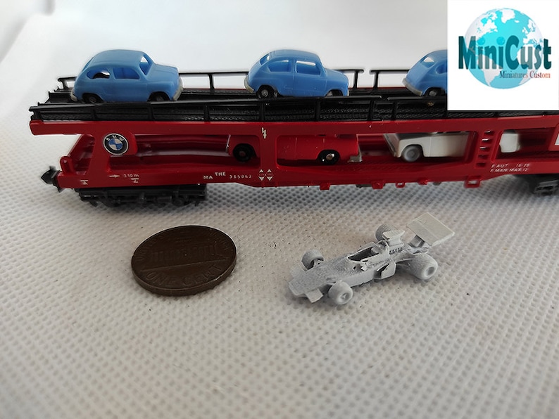 Puede incluir: Un vag&oacute;n de tren rojo de juguete con un logotipo BMW azul y tres coches de juguete azules en una plataforma. El vag&oacute;n de tren tiene el texto "THE MA 133061" impreso en el lateral. Un coche de carreras blanco de juguete est&aacute; sobre una superficie blanca.
