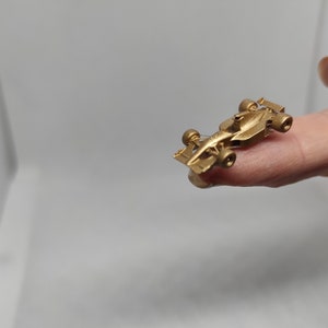 Puede incluir: Un modelo de coche de carreras en miniatura de color dorado. El coche es muy peque&ntilde;o y se sostiene en un dedo.