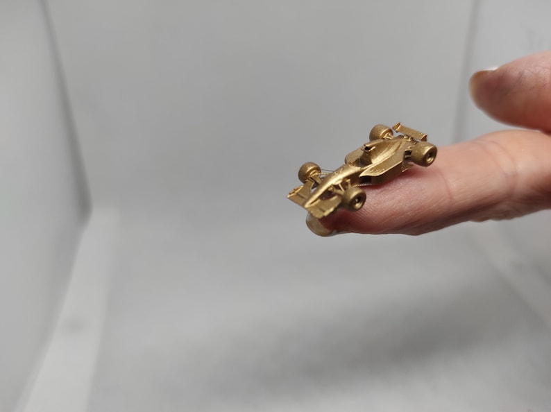Puede incluir: Un modelo de coche de carreras en miniatura de color dorado. El coche es muy peque&ntilde;o y se sostiene en un dedo.