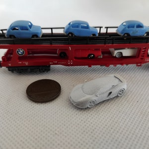 Puede incluir: Un vag&oacute;n de tren rojo de juguete con un marco de metal negro y un coche blanco en el nivel superior. El vag&oacute;n lleva cuatro coches de juguete azules. El vag&oacute;n tiene el texto "THE" y "MA 335611" impreso en el lateral. Un coche de juguete blanco est&aacute; en el suelo delante del vag&oacute;n.