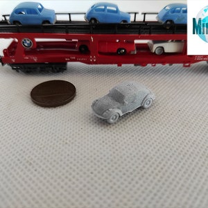 Puede incluir: Un coche modelo gris sobre una superficie blanca. El coche es un Volkswagen Beetle cl&aacute;sico de forma redondeada y tama&ntilde;o peque&ntilde;o. El coche est&aacute; sobre una superficie blanca con un patr&oacute;n texturizado. El coche es un modelo en miniatura y tiene aproximadamente el tama&ntilde;o de una moneda de un centavo.