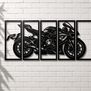 Può includere: Arte da parete in metallo nero raffigurante una motocicletta, suddivisa in cinque pannelli incorniciati. Il design include ruote, dettagli del motore e la lettera "R". L'opera è montata su un muro di mattoni bianchi.
