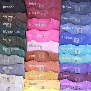 May include: A collection of Comfort Colors t-shirts in various colors, including black, red, and neon pink. Each shirt is neatly folded, showcasing the different hues available. The image displays a wide array of colors, with labels identifying each shade.