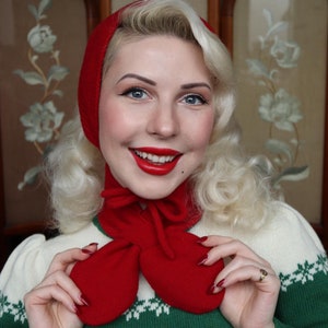 Könnte beinhalten: Eine Frau mit blonden Haaren trägt eine rote Strickmütze und einen Schal mit einem grün-weißen Pullover.