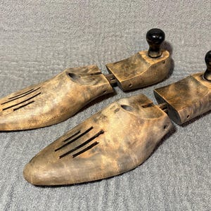 May include: A pair of wooden shoe trees with a brown finish. The shoe trees have a rounded shape and are designed to help maintain the shape of shoes.