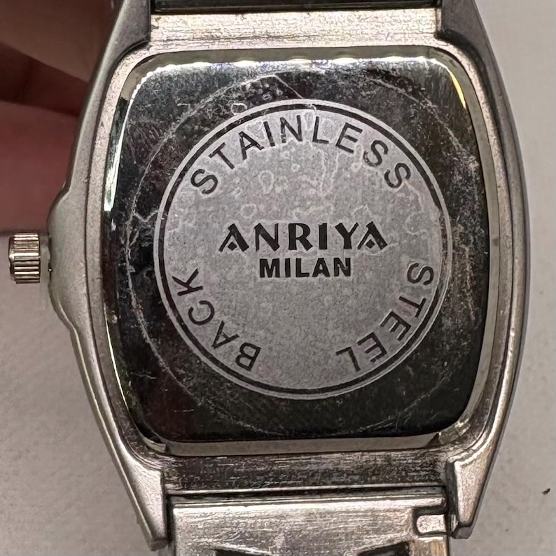 Pode incluir: Rel&oacute;gio prateado com mostrador quadrado e fundo de a&ccedil;o inoxid&aacute;vel. A parte de tr&aacute;s do rel&oacute;gio tem as palavras "STAINLESS STEEL BACK" e "ANRIYA MILAN" impressas.