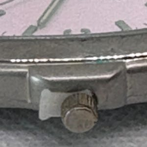 Pode incluir: Close-up de uma pulseira de rel&oacute;gio prateada com um pequeno bot&atilde;o redondo prateado. O bot&atilde;o tem uma superf&iacute;cie texturizada.