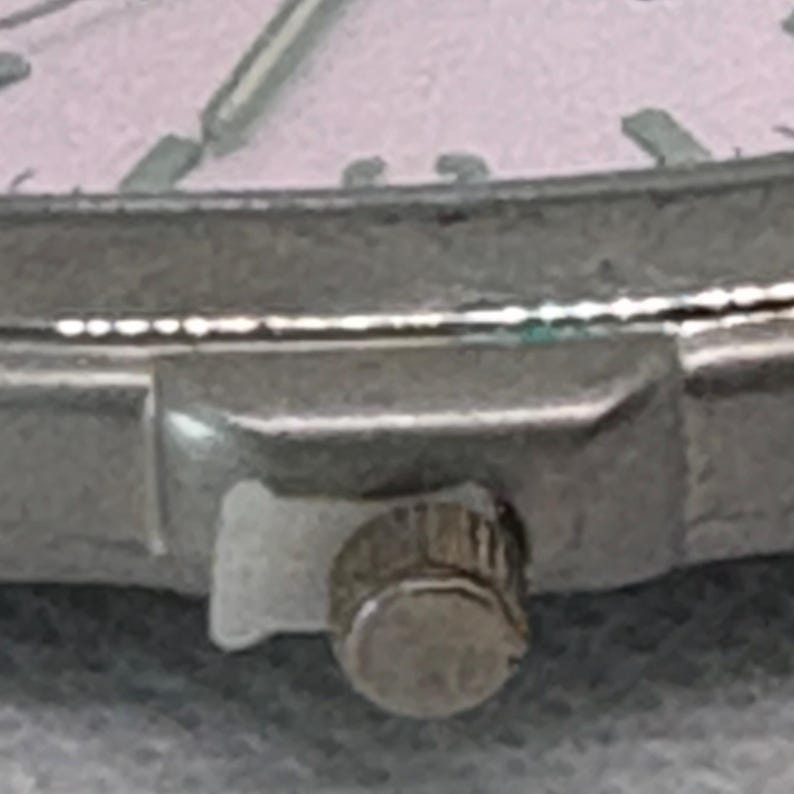 Pode incluir: Close-up de uma pulseira de rel&oacute;gio prateada com um pequeno bot&atilde;o redondo prateado. O bot&atilde;o tem uma superf&iacute;cie texturizada.