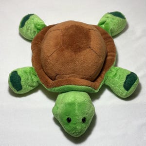 May include: A plush turtle toy with a brown shell and green limbs and head. The turtle's shell is a darker brown, and the limbs and head are a vibrant green. The toy has small, black eyes.