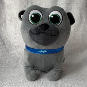 May include: Gray plush toy of a pug with large, green eyes and a blue collar with a lightning bolt design.