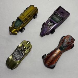 Peut inclure: Quatre voitures jouets vintage en or, violet, orange et jaune. Les voitures ont des roues noires et divers degrés d'usure de la peinture. Les voitures sont en métal moulé sous pression et semblent dater des années 1960 ou 1970.