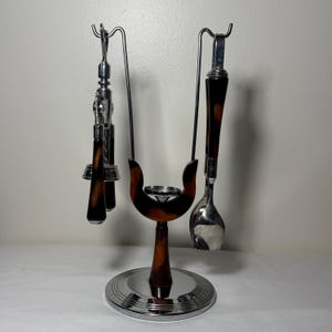 May include: A vintage bar tool set with a chrome base and accents. The set includes a corkscrew, spoon, and other tools with brown and black patterned handles. The tools hang from a decorative stand.