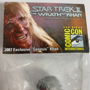 Puede incluir: Una bolsa de plástico que contiene una pequeña figura de acción gris y roja de "Genesis" Khan de la película Star Trek II: La Ira de Khan. La bolsa tiene una pegatina de Comic-Con International 2007 y el texto "2007 Exclusive "Genesis" Khan" impreso en ella.
