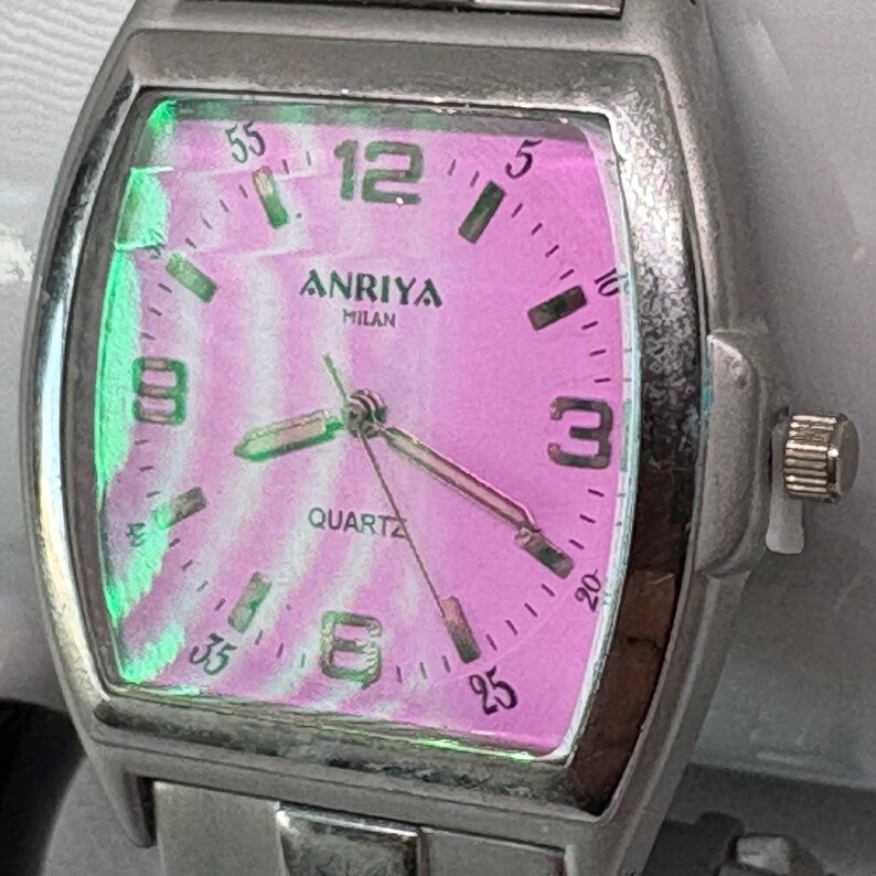Pode incluir: Um rel&oacute;gio de pulso prateado com um mostrador rosa e n&uacute;meros pretos. O mostrador do rel&oacute;gio diz "Anriya Milan Quartz".