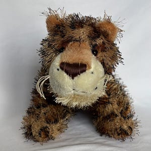 May include: A brown and black plush tiger with a white face and brown nose. The tiger has a fluffy texture and is lying down.