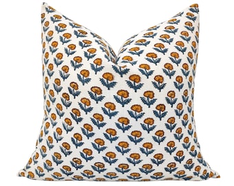May include: A white cushion with a floral pattern in shades of orange and blue. The cushion is made of a soft, comfortable fabric and is perfect for adding a touch of colour and style to any room.