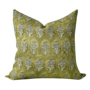 May include: A square throw pillow in a muted olive green color featuring a repeating pattern of small, light blue and white floral motifs arranged in vertical rows across the entire surface of the fabric, creating a consistent botanical design.