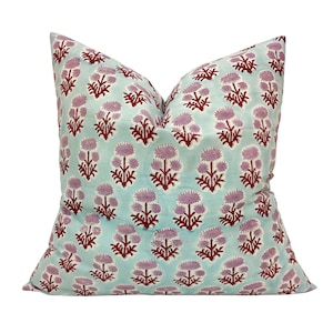 Pode incluir: Uma almofada azul claro com um padrão floral vermelho e rosa. A almofada é feita de algodão e tem uma forma quadrada.