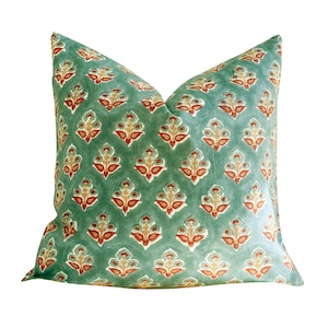 May include: A square throw pillow featuring a sage green background with a repeating pattern of stylized floral motifs in shades of orange, cream, and teal. The fabric displays a soft, matte texture with a consistent, symmetrical botanical print.