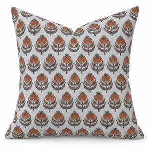 May include: A square throw pillow featuring a repeating floral pattern. The design consists of stylized orange and dark gray flowers with green accents arranged in vertical rows against a solid off-white background, creating a balanced look.