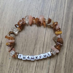 May include: A brown and pink gemstone bracelet with the word "THANKFUL" spelled out in white letter beads.