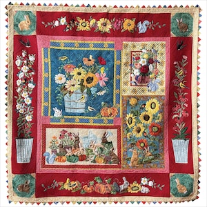 Può includere: Una trapunta artigianale con sfondo rosso e vari pannelli ricamati. I pannelli presentano composizioni floreali, conigli, scoiattoli e uccelli. La trapunta ha un bordo smerlato con un motivo triangolare ripetuto.