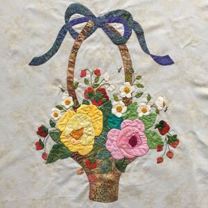 May include: A brown wicker basket with a blue bow is filled with a variety of flowers, including yellow roses, pink roses, and white flowers. The basket is surrounded by green leaves and red strawberries.