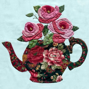 Op de afbeelding: Een vintage-theepot met een bloemenpatroon, gevuld met roze en rode rozen. De theepot is gemaakt van stof en heeft een handvat en een tuit.