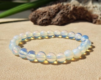 Könnte beinhalten: Ein weißes Opal-Perlenarmband mit irisierendem Schimmer. Das Armband besteht aus runden Perlen und ist auf einem Gummiband gefädelt.