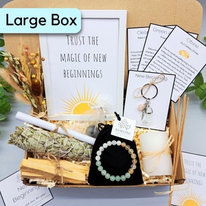 May include: A large box filled with spiritual items. Includes a framed print with the text "Trust the Magic of New Beginnings", a sage bundle, palo santo sticks, a bracelet, a candle, and cards with text.