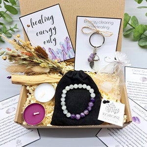 May include: A gift box filled with healing crystals, candles, and other items. The box includes a selenite crystal, amethyst bracelet, clear quartz, palo santo stick, and two candles. The box also includes a card that says "healing energy only" and a keychain with an amethyst crystal and a feather charm.