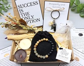 May include: A gift box with a variety of items, including a bracelet, keychain, candles, and dried flowers. The box contains a bracelet with light brown and black beads, a keychain with a black stone, and a card that says "Success is the only option."