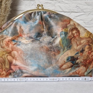 Könnte beinhalten: Eine Clutch-Tasche mit goldenem Verschluss und einem Stoff mit einem Gemälde im Renaissance-Stil mit Figuren in Blau-, Pfirsich- und Goldtönen. Die Tasche ist etwa 35 cm breit.