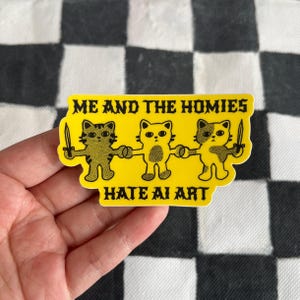 May include: A yellow sticker with the text "ME AND THE HOMIES HATE AI ART." The sticker features three cartoon cat figures holding hands and knives. The cats are in various shades of brown and yellow.