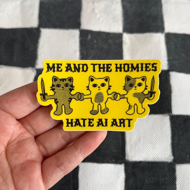 May include: A yellow sticker with the text "ME AND THE HOMIES HATE AI ART." The sticker features three cartoon cat figures holding hands and knives. The cats are in various shades of brown and yellow.