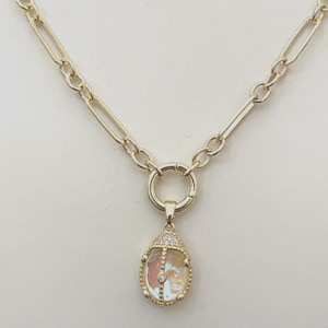 May include: Gold-coloured necklace with a teardrop pendant. The pendant has iridescent glass and a diamond accent. The chain has oval and rectangular links. The pendant is framed with a beaded edge and a pave-set bail.