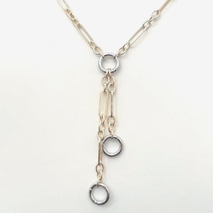 May include: Silver-toned necklace with a Y-shaped design. The necklace features a series of small, linked chains and two dangling circular pendants. The design includes a mix of oval and rectangular links.