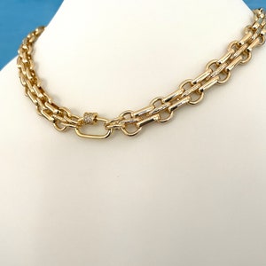 May include: A gold chain necklace with a double row of interlocking links and a small, diamond-encrusted clasp.