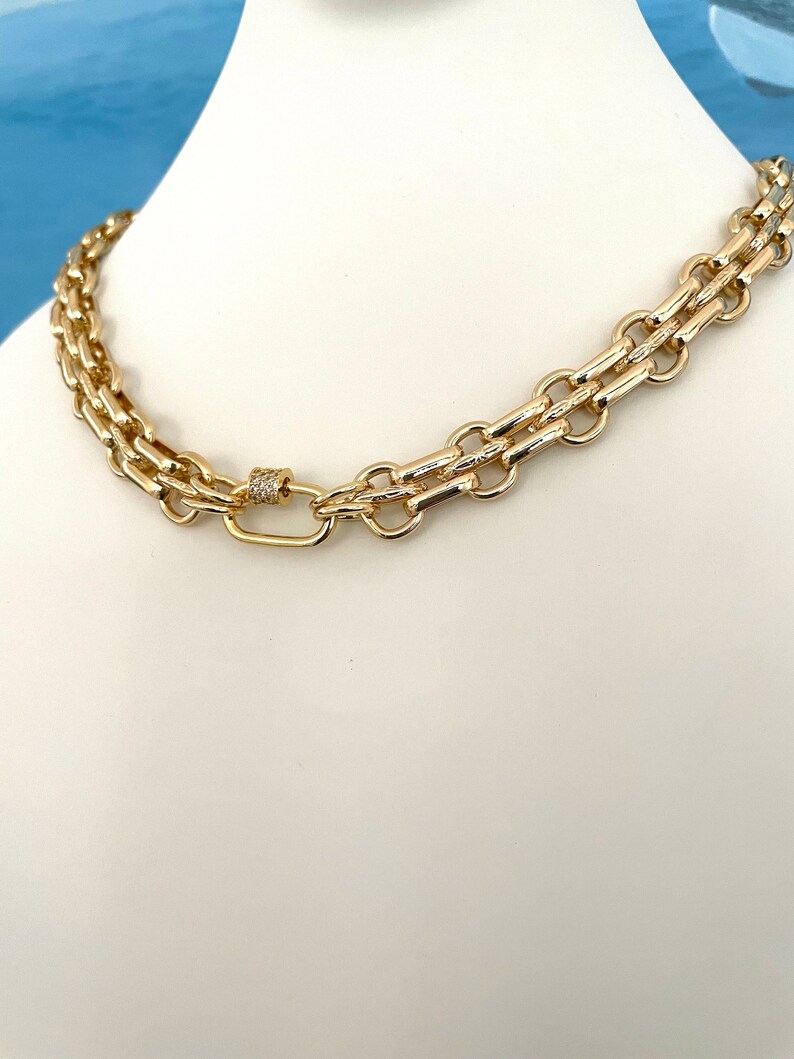 May include: A gold chain necklace with a double row of interlocking links and a small, diamond-encrusted clasp.