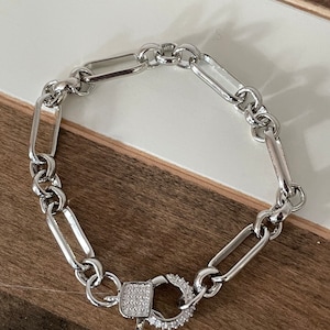May include: A silver chain bracelet with a silver clasp that is encrusted with small clear stones.
